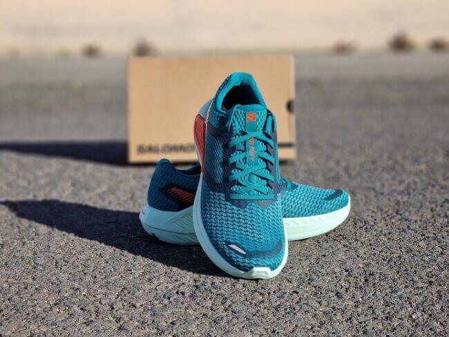 Présentation des chaussures de running Salomon DRX Defy. Les chaussures sont présentées sur le bitume, devant une boite à chaussures Salomon.