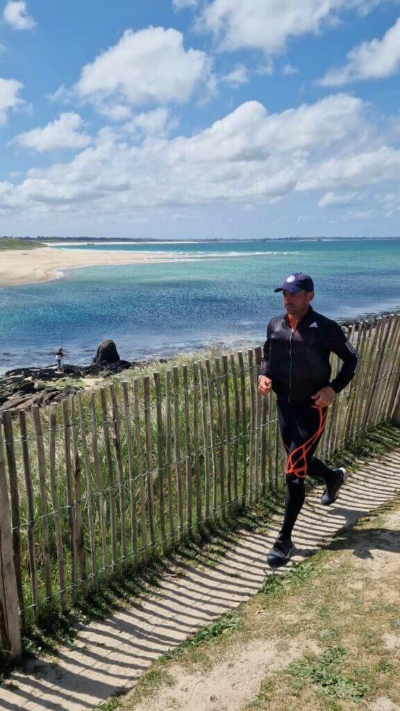 Erik Clavery courant sur le GR34 avec en toile de fond une crique bretonne
